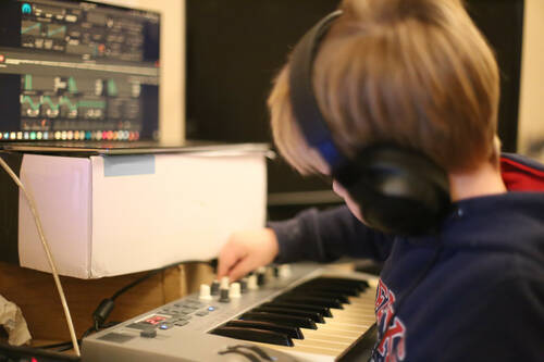 A kid playing with a keyboard in front of a computer