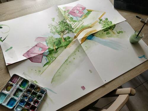 Aquarelle of a small village with an isometric view. Placed on a table with brushes and painting around.